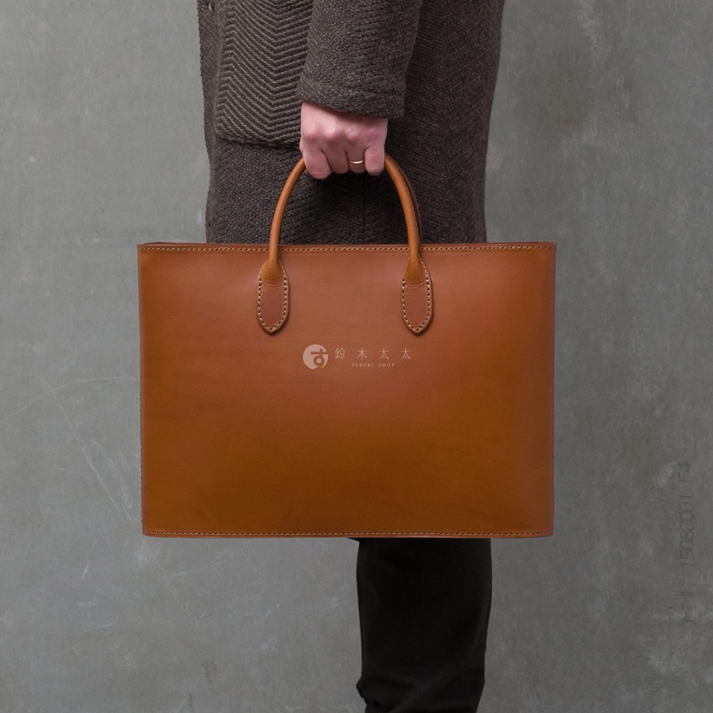 職人手作的棕色皮革薄型公事包，配有雙提把，中央有品牌Logo。