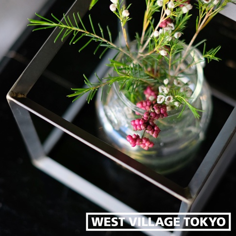 一個由銀灰色鐵製成的長方體框架，內部有一個玻璃花瓶，瓶中插有綠色細長的葉子和粉紅色、白色的小花苞。