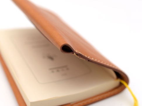 職人手作皮革翻蓋記事本書套，L尺寸，採用淺棕色皮革製成，質感細膩。書套翻蓋處有精緻縫線，內含淺色內頁筆記本，並附有黃色書籤帶。