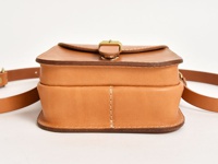 淺棕色皮革翻蓋迷你單肩包，設有金色金屬扣，搭配皮革肩帶，包身線條簡潔，手工縫線清晰可見。