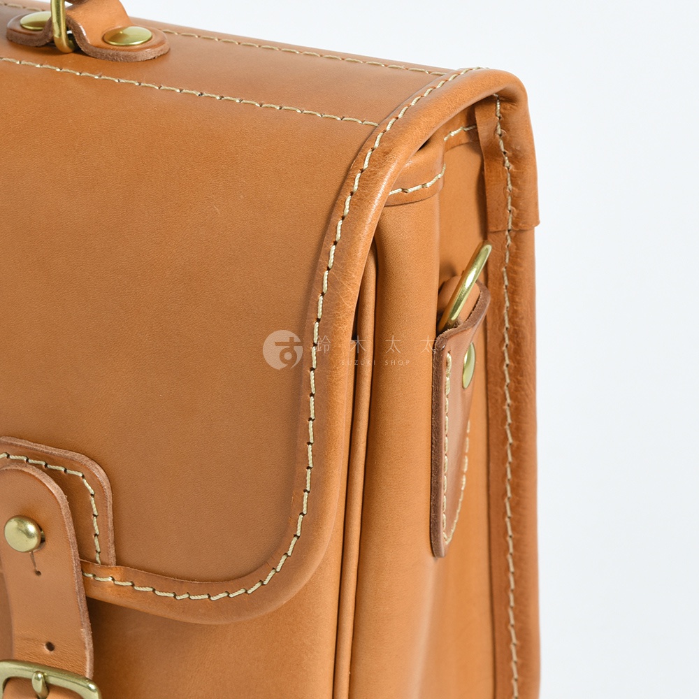 職人手作皮革商務休閒兩用單肩包，採用溫暖的棕褐色皮革，搭配精緻的米白色縫線，展現復古質感。包身設有金屬釦環和皮質繫帶，設計簡潔實用。