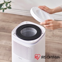 情境式空氣清淨機 IAP-A25 頂部特寫，顯示已取出圓形白色頂蓋，露出內部黑色的濾網組件。機身為白色，側邊有密集的圓形透氣孔。