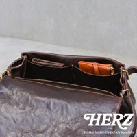 深棕色皮革斜背包內部，可見卡夾和零錢包，包身結構清晰，縫線細緻，展現職人手作質感。