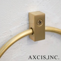 黃銅圓形毛巾環，固定於白色紋理牆壁上，呈現復古金色光澤，環狀部分由方形底座支撐，底座以螺絲固定。