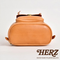 職人手作皮革經典後背包 R-4，展示的是一個淺棕色皮革後背包的底部和側面，呈現圓潤飽滿的曲線，頂部有深棕色皮革裝飾和金屬扣環。