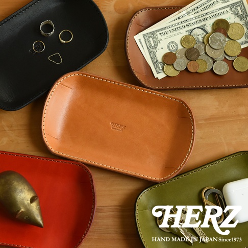 職人手作皮革小物收納盤，共五色：黑色、原色、紅色、棕色、綠色。盤中展示戒指、美金、硬幣、鑰匙、AirPods等物品，材質為皮革，縫線精緻。