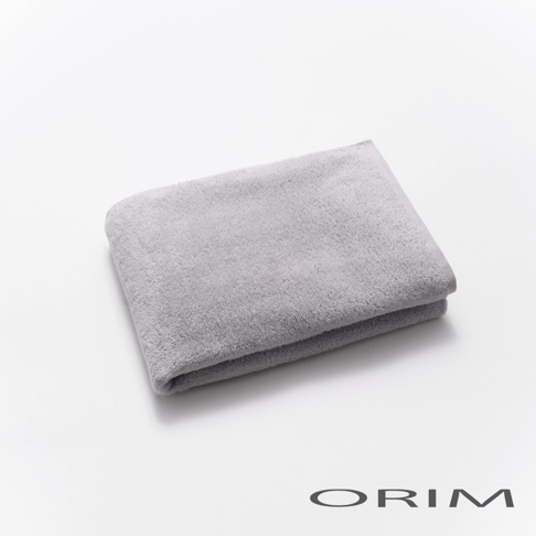 一條折疊的淺灰色浴巾，材質柔軟，表面有細緻的絨毛，置於白色背景上，右下角有 ORIM 標誌。