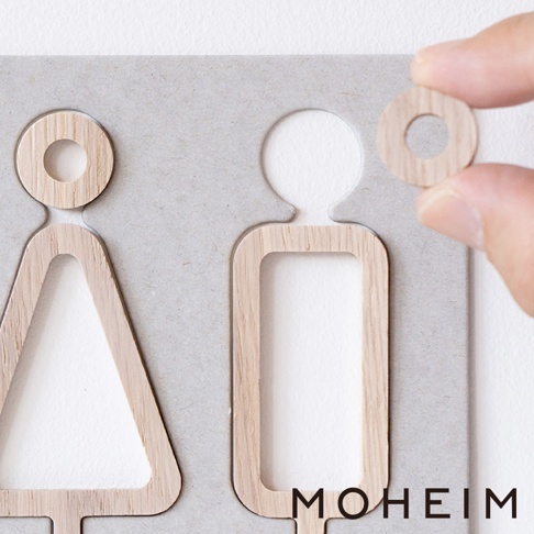 木製男女標示牌，包含三角形（代表女性）和方形（代表男性）的木質鏤空設計，置於淺灰色背景板上。