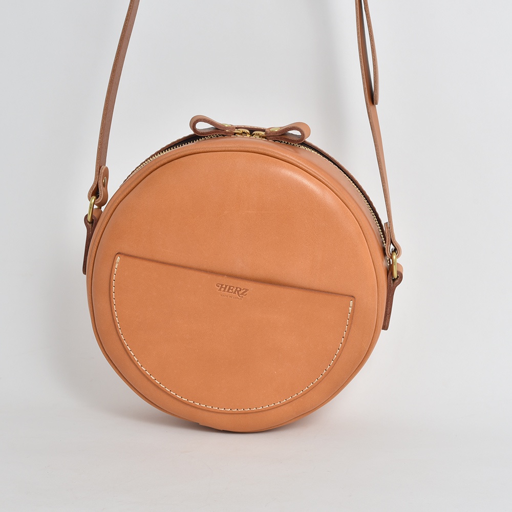 職人手作皮革小圓包 CK-19 M，淺棕色，圓形設計，正面有半月形口袋，搭配可調式皮革背帶，拉鍊開合，品牌標誌壓印在口袋上。