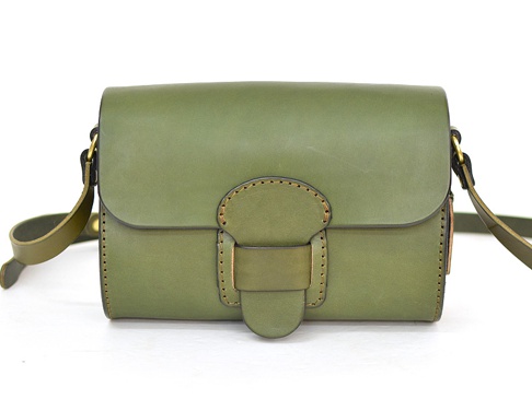 一綠色皮革馬鞍包，配有寬版可調式肩帶及金屬寬扣帶，包身縫線明顯，設計簡約。