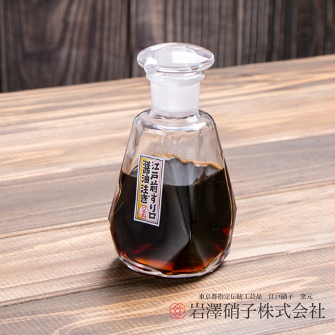 透明玻璃醬油瓶，瓶身呈不規則多邊形，裝有深褐色醬油，瓶口配有白色塞子和透明玻璃蓋。瓶身貼有日文標籤。