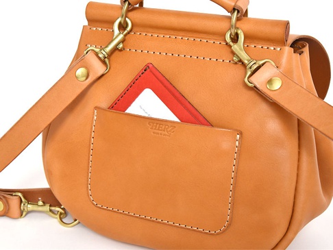 職人手作皮革屋瓦風迷你後背包 (R-6)，採用天然棕色皮革製成，設有外袋，可見紅色卡夾露出。包包有金屬釦環和皮革背帶，展現精緻工藝。