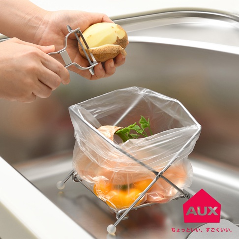 銀色金屬材質的折疊式垃圾架，架上套著透明塑膠袋，袋內有洋蔥、黃椒和芹菜葉。架子下方有白色圓形腳墊。