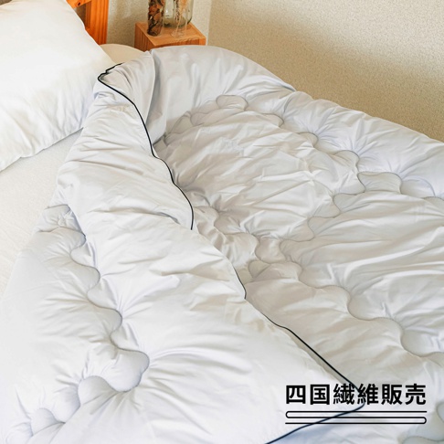 一張雙人白色空氣暖被，被子表面有波浪形縫線，邊緣飾有黑色滾邊，鋪在床上，旁邊放著一個白色枕頭。