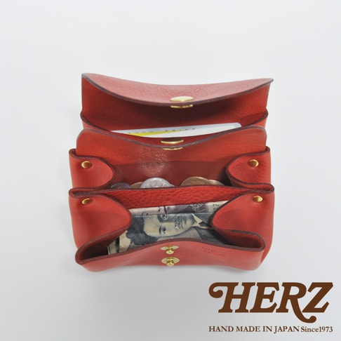 紅色皮革三層收納零錢包，內有硬幣、紙鈔和卡片，採用金屬按扣開合，皮革表面有紋理，展現職人手作質感。
