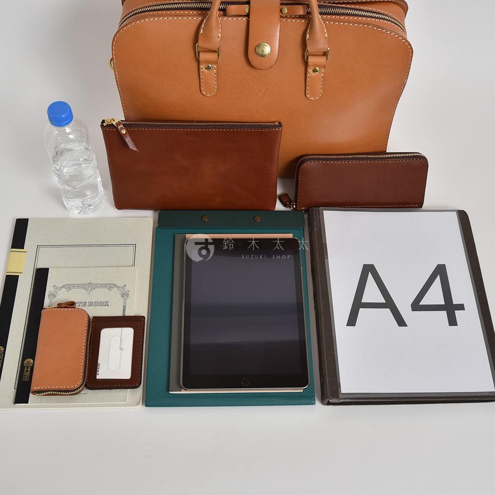 棕色皮革公事包，內含多個收納隔層。包內展示一個棕色拉鍊夾、一個小型棕色零錢包、兩本筆記本、一個卡夾、一台平板電腦和一張 A4 紙。