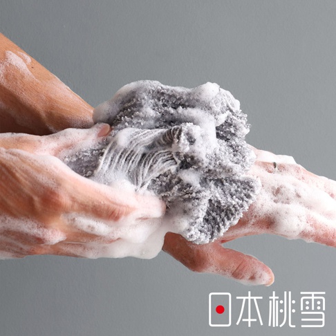 日本人手搓洗沐浴巾，產生豐富泡沫，背景為灰色牆面，右下角有「日本桃雪」的日文標誌