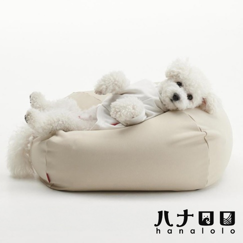 一隻白色比熊犬正慵懶地躺在米色方形懶骨頭沙發上，狗狗面向鏡頭，下方標示著日本hanalolo品牌名稱，整體呈現舒適放鬆的居家氛圍。