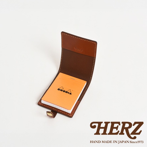 職人手作皮革便利貼收納套，咖啡色皮革製成，可容納橘色 Rhodia 便利貼，翻蓋式設計，附有金色扣環。