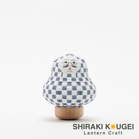 達摩不倒翁造型迷你提燈，燈身為白色紙質，印有藍色棋格紋圖案，臉部繪有黑色鬍鬚、眼睛和嘴巴。提燈底部為圓形木質底座。