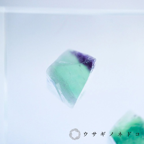 螢石八面體標本，厚切片狀，呈現漸層的淺綠色與紫色，材質為天然礦石，表面光滑，置於淺色背景前。