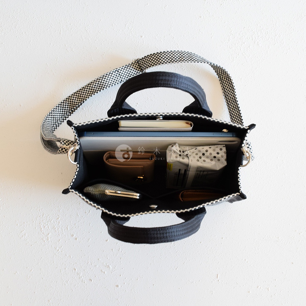 三河木綿刺子織兩用方形托特包，黑色與白色格紋肩帶，包內裝有筆記本、錢包、手機及紙巾包。