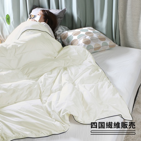 一床米白色雲絨被，被面有明顯的絎縫紋路，柔軟蓬鬆，覆蓋在床上，一旁有印有圓形圖案的枕頭。