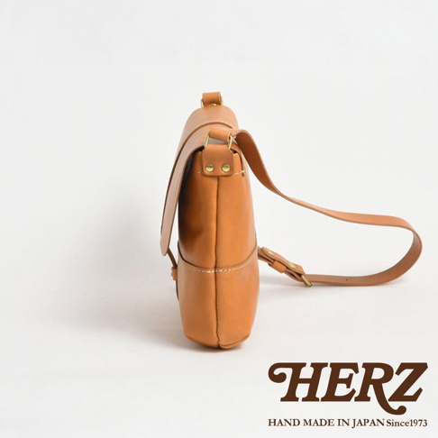 日本HERZ品牌手作皮革細扣帶馬鞍包，淺棕色皮革，側視圖，下方為HERZ品牌標誌與「HAND MADE IN JAPAN Since1973」字樣