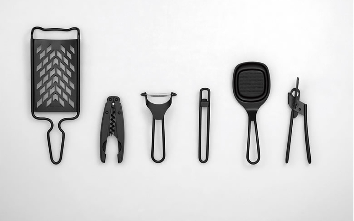 黑色廚具組，包含刨絲器、開瓶器、削皮器、刮刀及夾子，皆為金屬或塑膠材質，設計簡潔。