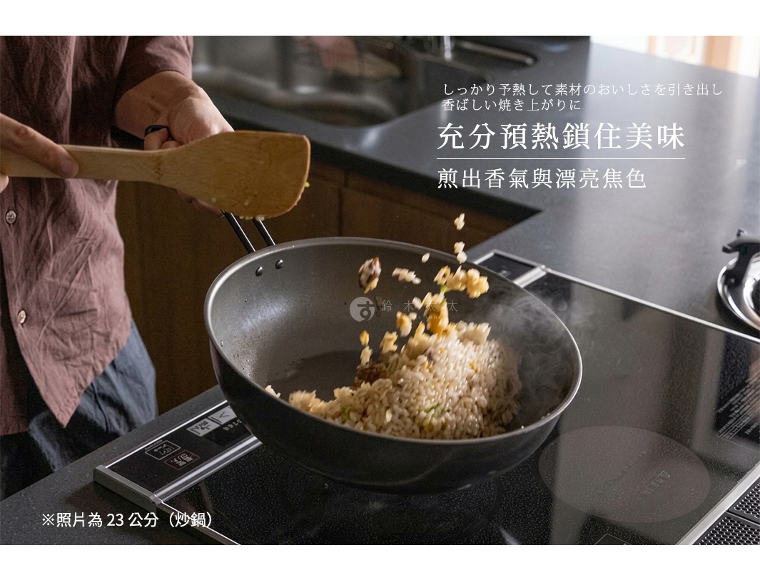 一位穿著棕色襯衫的人正在黑色電磁爐上使用木製鍋鏟翻炒平底鍋內的炒飯。鐵製平底鍋呈現深灰色金屬質感，鍋中炒飯正熱氣騰騰地拋起。圖片上方以日文與中文寫著關於充分預熱以鎖住食材美味與煎出漂亮焦色的標題，下方註明照片所示為23公分炒鍋。