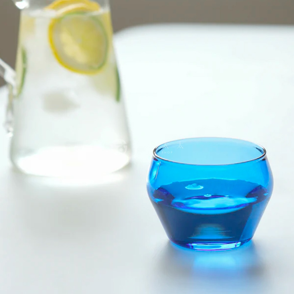 LAGOM 清透復古圓潤玻璃杯，採用藍色玻璃材質，杯身呈圓潤的復古造型，底部寬而向上收窄，盛有藍色液體，杯口邊緣有細微金屬質感的鑲邊。