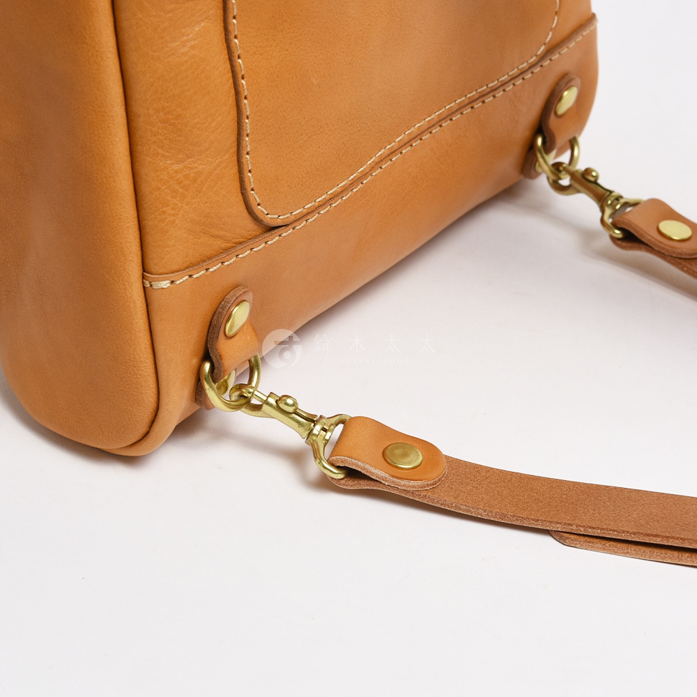 職人手作皮革大開口圓角後背包，展示棕褐色皮革材質、金色金屬釦環與鉤扣，以及縫線細節。