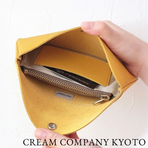 黃色皮革手拿包，內有拉鍊夾層，可放入卡片，包款外觀為簡約的信封式設計，以金屬按扣固定。