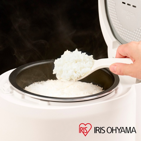 一隻手拿著勺子，正從一個白色的電鍋中舀出熱騰騰的白米飯，旁邊的電鍋內也裝著米飯，電鍋蓋子是打開的。