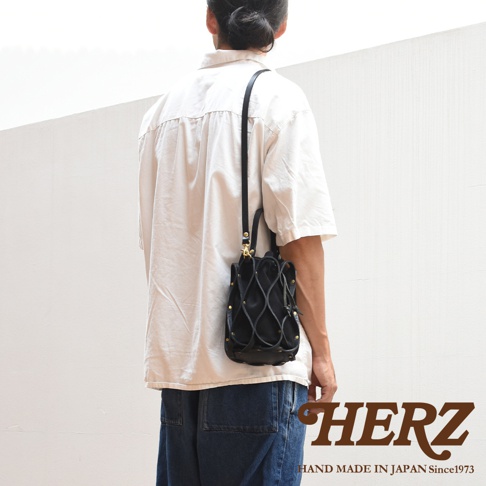 日本HERZ職人手作皮革Organ編織水桶包 G-98，模特身著淺色寬鬆襯衫和牛仔褲，展示此款黑色皮革編織水桶包的側背造型。