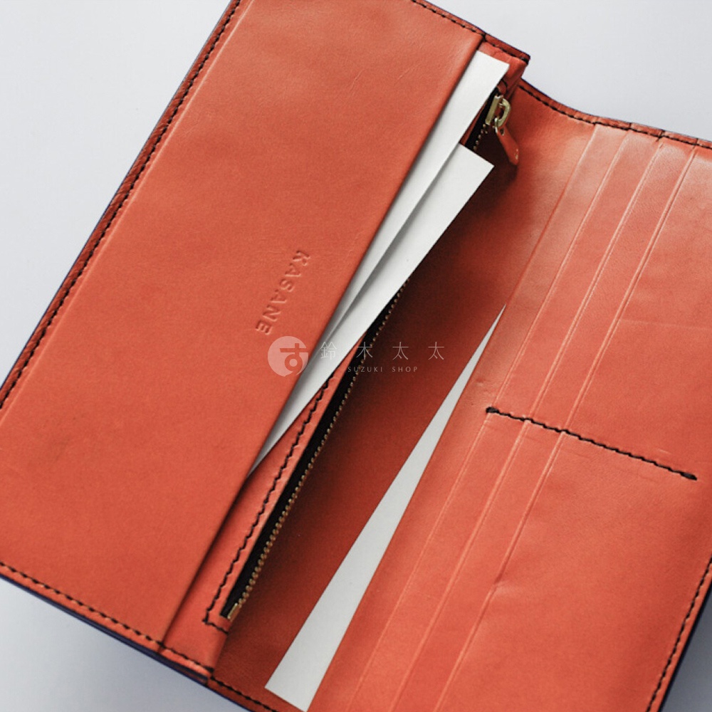 一個打開的橘棕色皮革長夾，內部露出夾層和卡片槽，並印有KASANE品牌字樣。