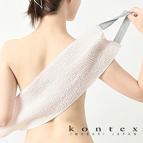 一條淺粉色、帶有織紋的天然素材按摩洗澡巾，配有灰色提帶，一端由人體背部伸出，另一端由手臂拉住。