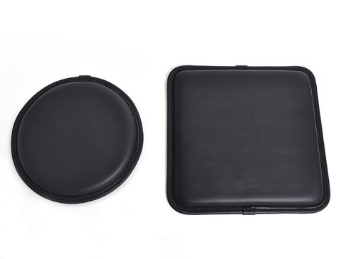 兩個黑色皮革坐墊，一個圓形，一個方形，均採用職人手作工藝，邊緣縫線精緻，材質光滑。