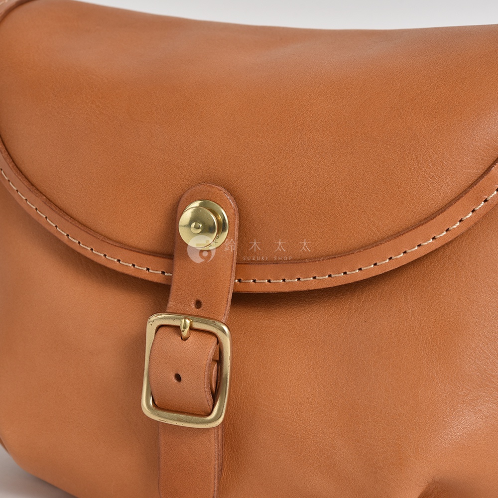 日本HERZ職人手作皮革休閒旅行馬鞍包的特寫，展示了焦糖色皮革、金屬釦環和縫線細節。
