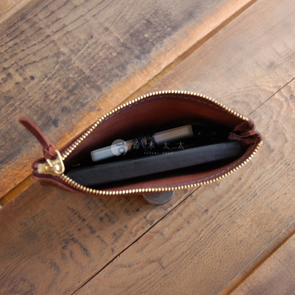 一個棕色皮革拉鍊式小物收納袋，內部有鑰匙、USB 隨身碟和一個黑色薄型物品。袋子採用黃銅拉鍊，搭配皮革拉環。