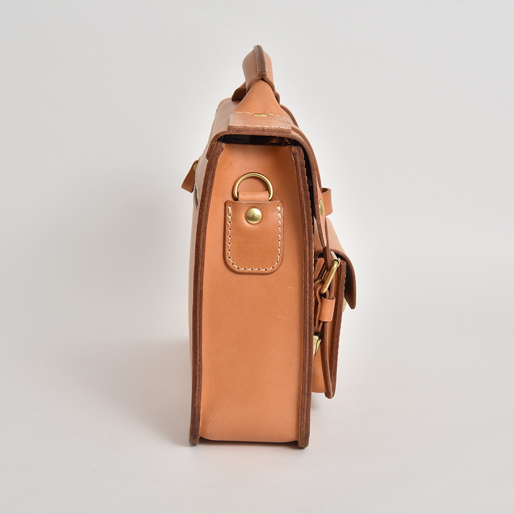 職人手作皮革學院風兩用公事包，天然皮革色，側邊視角，包款設計簡約，配有金屬扣環及皮革提把，展現皮革質感。