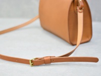 淺棕色皮革製成的極簡風拉鍊單肩包，帶有可調節長度的皮革肩帶和金色搭扣。