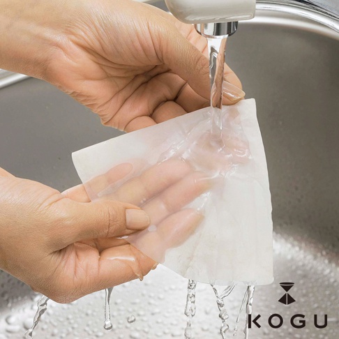 雙手正在水槽中沖洗白色錐形咖啡濾布，濾布材質輕薄，水流從濾布滴落。