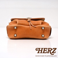 橘色皮革郵差包，有鹿角扣和皮革繩，底部有四個金屬鉚釘。