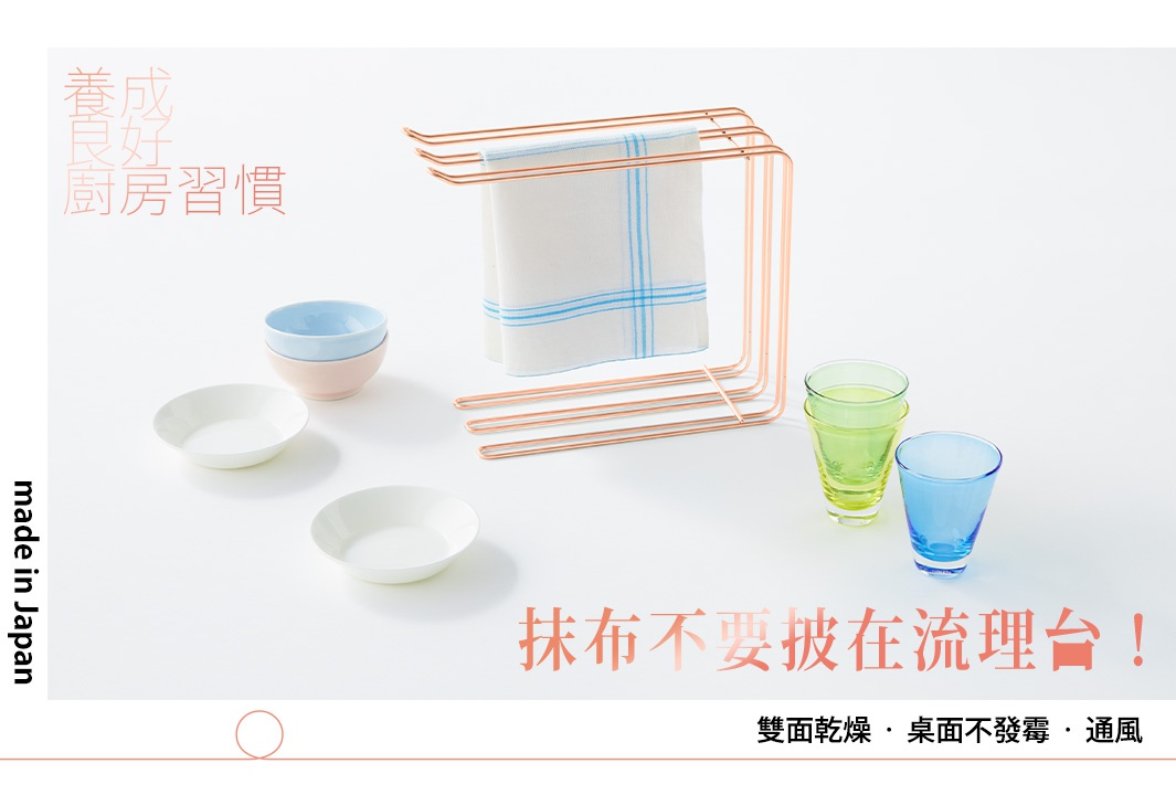 不鏽鋼三桿抹布架，玫瑰金。架上掛有白色帶藍色格紋的抹布。旁邊擺放著兩個白色盤子、兩個疊放的淺色碗，以及兩個玻璃杯，一個為淺綠色，一個為藍色。