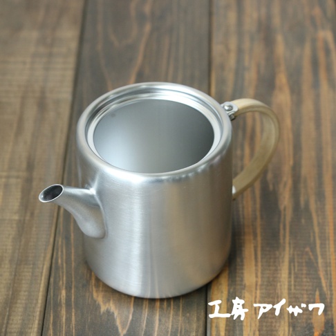 霧面不鏽鋼直筒茶壺，側邊附有淺色木質把手，壺身帶有細緻的金屬紋理，壺嘴向上傾斜。