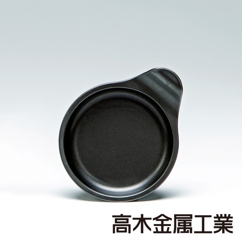 日本製黑色圓形烤盤，帶有一體式手柄，材質為金屬，表面呈細微顆粒狀，適合用於烤箱。