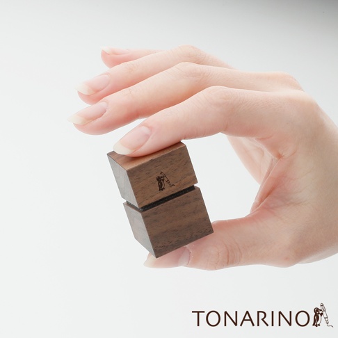 一雙手握著兩個深棕色天然實木製成的方形筆電散熱塊，其中一個散熱塊上刻有企鵝圖案。