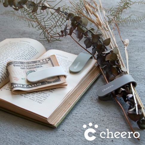 三款萬能QQ變形夾，分別為淺灰、淺綠和白色，皆為矽膠材質，印有「cheero」字樣，夾在裝有美鈔的書本和乾燥花束上。