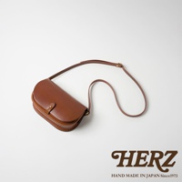 職人手作皮革迷你馬鞍包，呈現經典的半月形設計，選用光滑的棕色皮革，搭配可調節長度的細長肩帶，包身中央有一個小巧的按扣，整體散發日式職人質感。